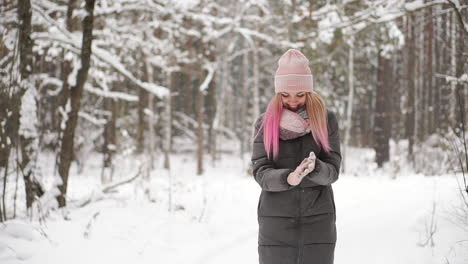 cámara lenta, una mujer con chaqueta, sombrero y bufanda en el invierno en el bosque sosteniendo nieve en sus manos y soplando hacia la cámara arroja nieve.