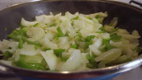 vapor saliendo de cebolla y pimiento verde en sartén, cierre lento