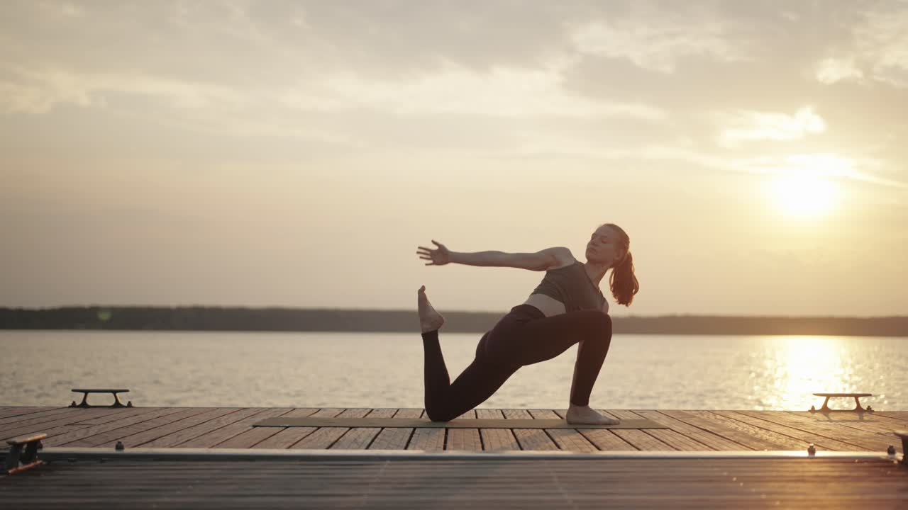 female yogi stretching legs on footbridge at lake at golden hour