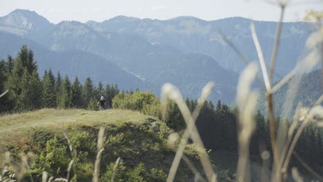 mountain biker pedalling up a ridge then stopping by a cliff in the alps