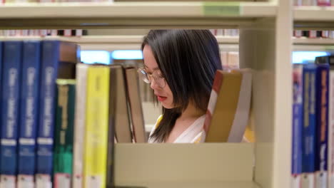 행복하고 즐거운, 예쁜 여성 학생의 초상화, 대학 도서관의 책장 배경에 앉아, 노트북과 배을 들고, 으로 바라보고, 즐겁게 미소 짓고.