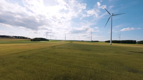 Green-fields-with-wind-turbines-on-sunny-day,-aerial-FPV-view