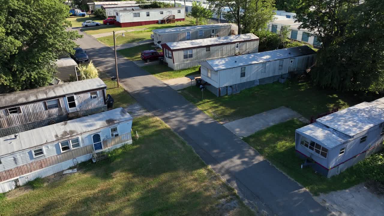Rusty roof of cheap mobile trailer home park in American suburb. Aerial flyover shot. Small garden and yards in low housing area of USA. Sunny summer day. Quiet scene. Poor district of town