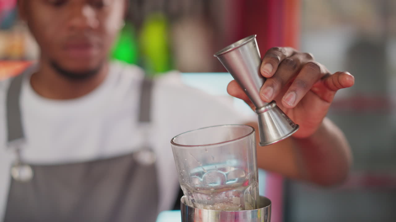 el camarero vierte licor del vaso en el bar de primer plano. el joven camarero prepara un cóctel para el cliente en el club nocturno. el hombre afroamericano hace una bebida