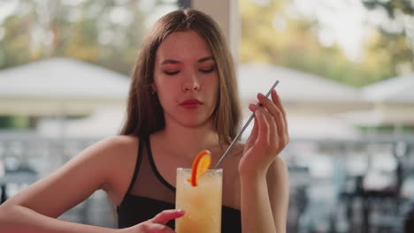 bored lady with cocktail sits in bar. young woman looks lonely resting in beach bar alone. female guest drinks exotic beverage with orange slice