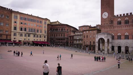 tourists explore siena's historic piazza del campo in italy on a quiet day under overcast skies