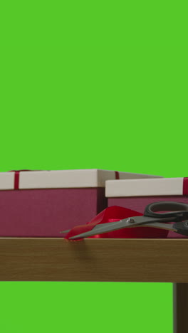 vertical video of man picking up present in gift wrapped box from table shot against green screen