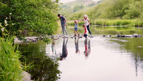 slow motion shot of parents helping children to cross river whilst hiking in uk lake district