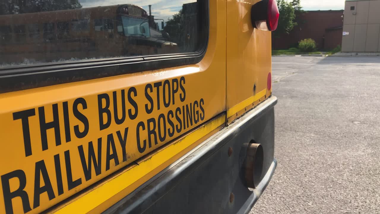 Avviso di cautela sul retro di uno scuolabus: QUESTO AUTOBUS SI FERMA AI PASSAGGI A LIVELLO