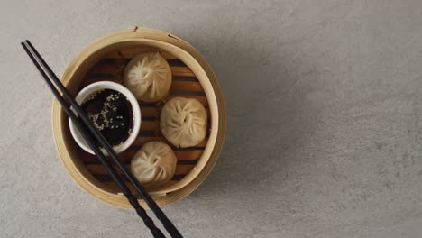 composition of bamboo steamer with dim sum dumplings and chopstick with soy sauce on grey background