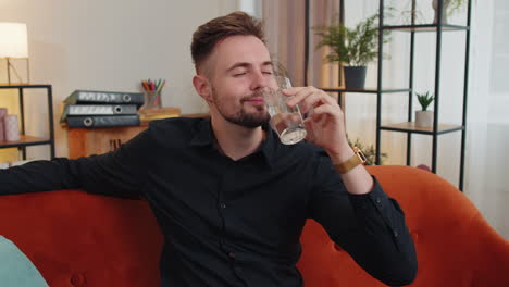 sediento un joven sentado en casa sosteniendo un vaso de agua natural hacer sorbos bebiendo agua tranquila