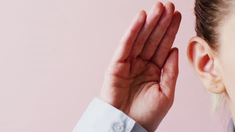 detalle de video de una mujer caucásica cubriendo la mano detrás de la oreja para escuchar más claramente, con espacio de copia rosa