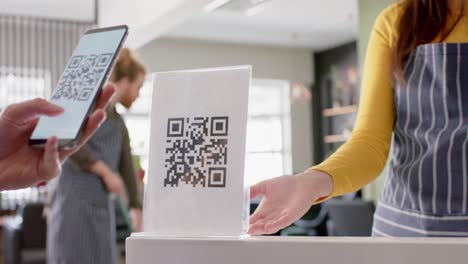 midsection of caucasian female hairdresser and client using qr code with smartphone, in slow motion