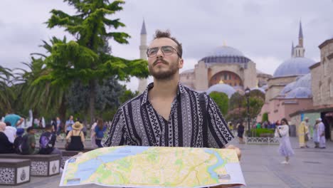 un joven está caminando mirando un mapa de papel en su mano.