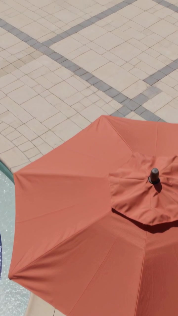 Vertical video: Shifting camera showing orange umbrella appearing smaller while revealing pool edge