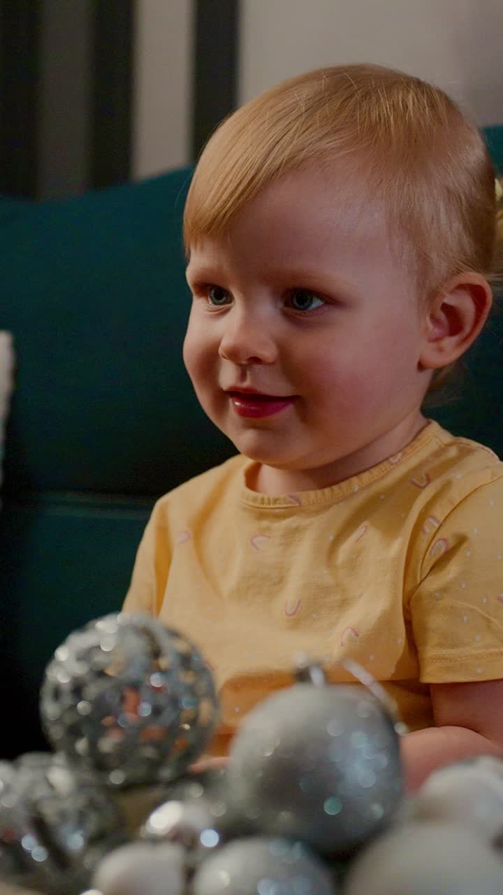A Delightful Child Enjoys Festive Holiday Decorations with Sparkling Ornaments, Capturing the Joy of Celebration in a Cozy Indoor Setting Surrounded by Glossy Christmas Baubles