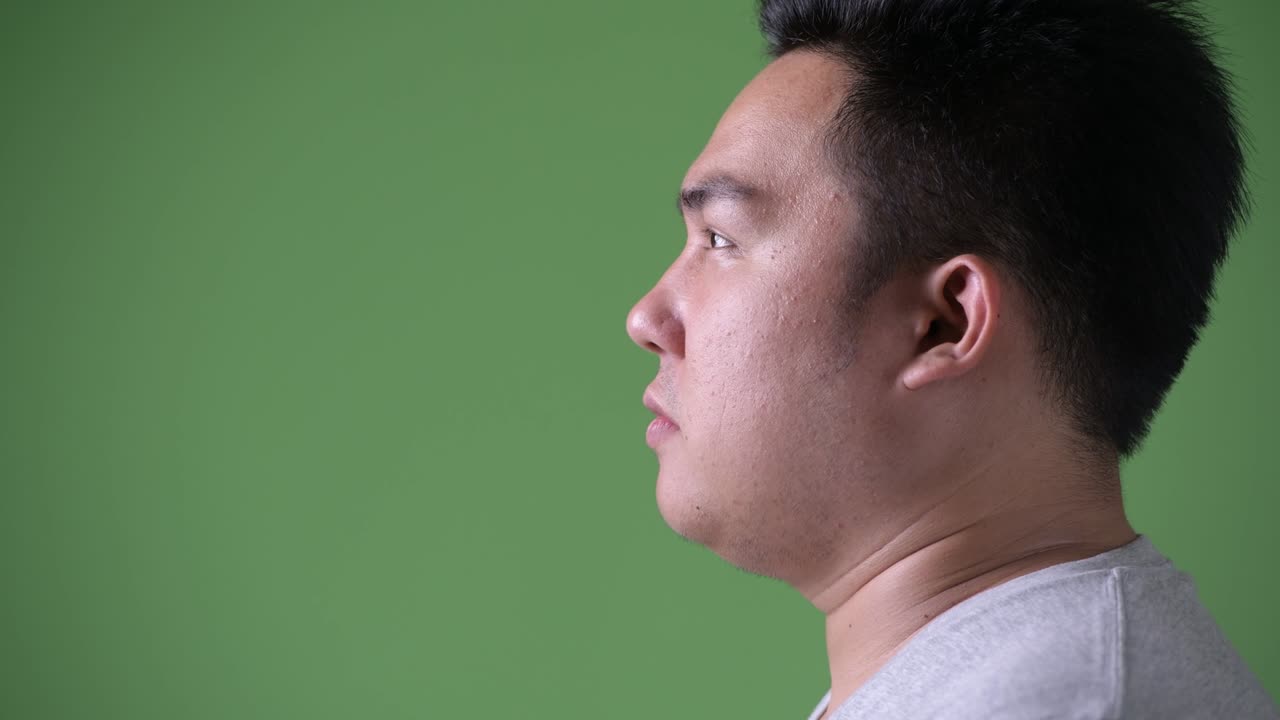 Young handsome overweight Asian man against green background