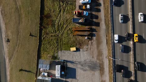 A-top-down-view-over-a-construction-site-with-vehicles-and-equipment-between-the-Belt-Parkway-and-a-park-in-Brooklyn,-NY-on-a-sunny-day