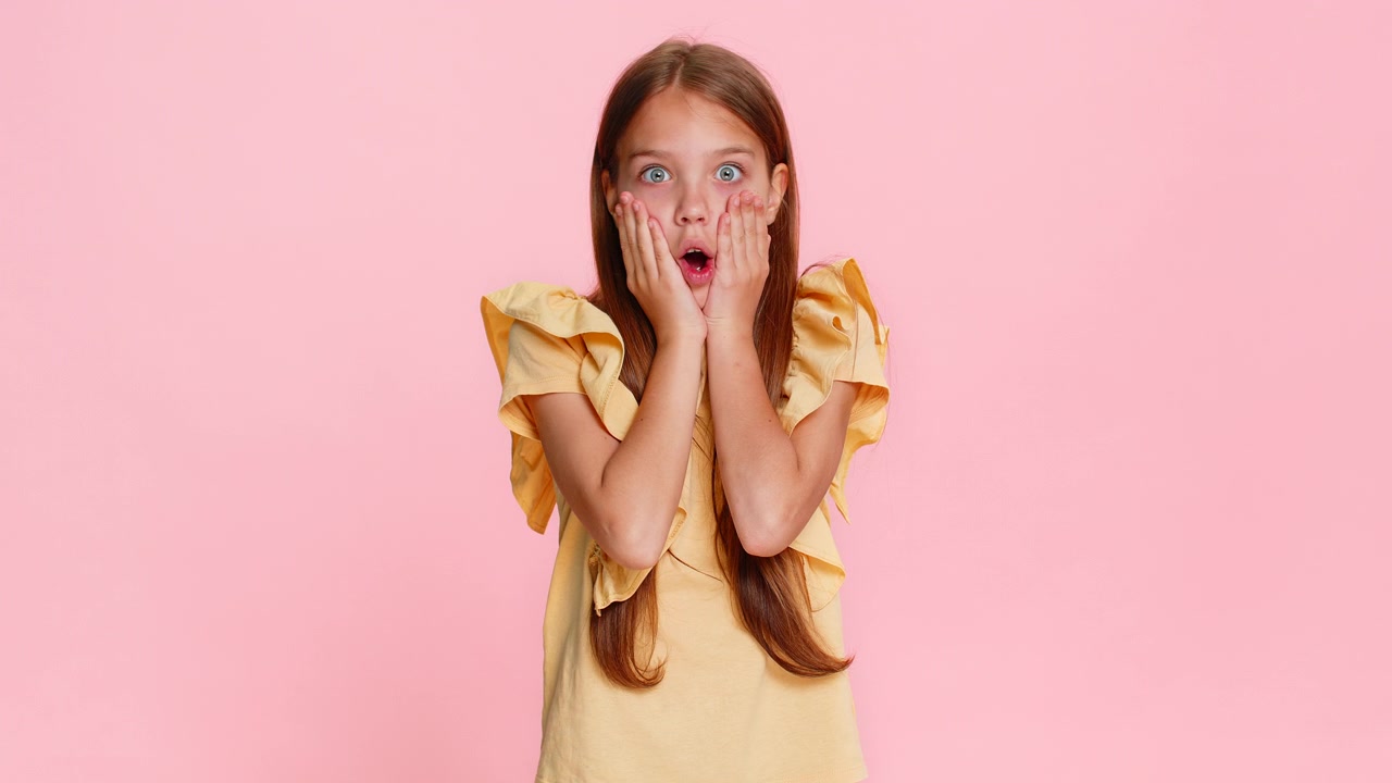 Child girl kid expressing surprise with open mouth and hands on cheeks in wow reaction pose