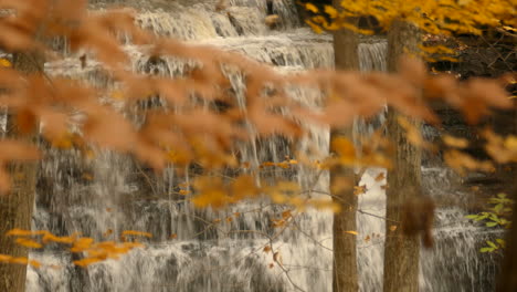 Cascada-Rocosa-A-Través-De-Hojas-De-Color-Otoñal-Balanceándose-Suavemente-En-El-Viento,-Cámara-Lenta