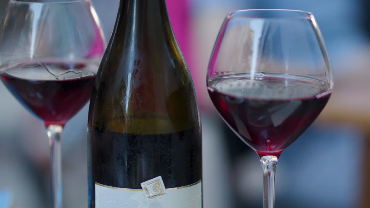 Movimento della fotocamera che supera un bicchiere di vino rosso e una bottiglia su un tavolo da pranzo all'aperto sfocato, illuminazione naturale