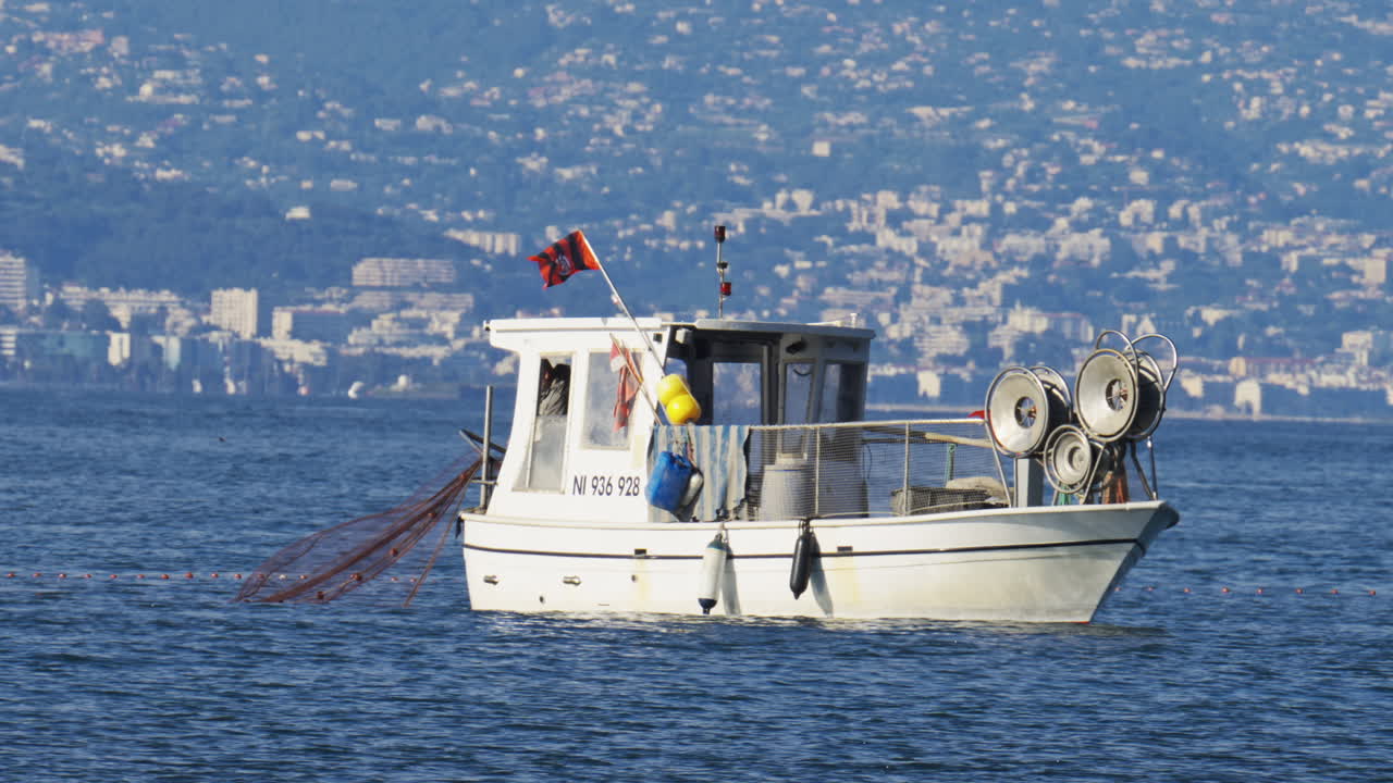 Antibes, Francia - 2 maggio 2025: vista di un uomo su una barca bianca che getta una rete da pesca nell'acqua blu in pieno giorno