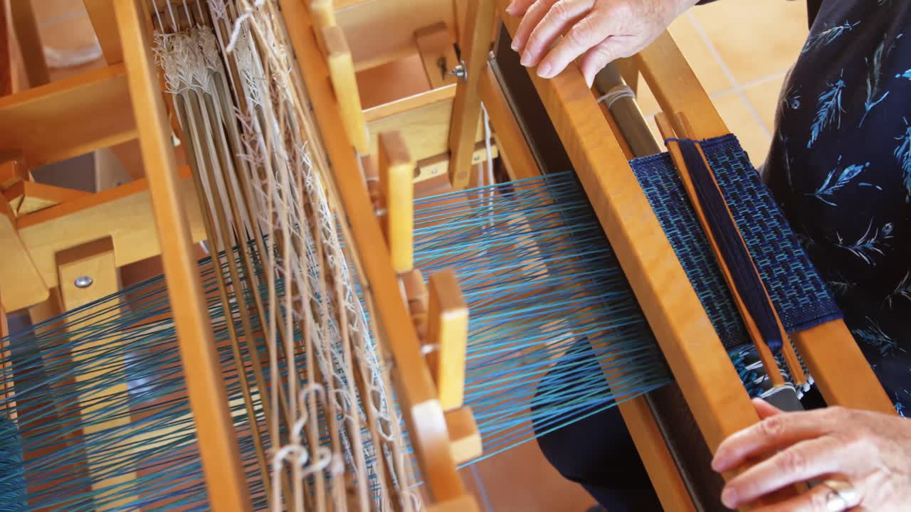 High angle view of old caucasian senior woman weaving cloth on handloom machine in a workshop 4k