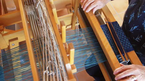 High-angle-view-of-old-caucasian-senior-woman-weaving-cloth-on-handloom-machine-in-a-workshop-4k