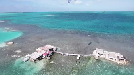 Luftaufnahme-Mann-Springt-Auf-Hölzernen-Alten-Pier-Vom-Stelzenhaus-Palafito-Los-Roques-Venezuela