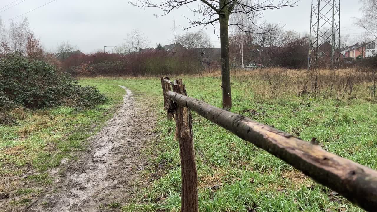 pequeña valla de madera hecha de troncos de árboles en un prado con árboles y pequeñas casas en el fondo