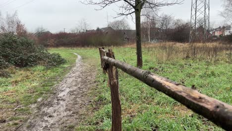 Small-wooden-fence-made-of-tree-trunks-on-a-meadow-with-trees-and-small-houses-in-the-background