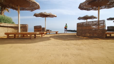 Steadicam-Shot-Mujer-De-Pie-En-La-Playa-Cerca-De-Las-Sombrillas-Y-Las-Palmeras-Mirando-Al-Mar