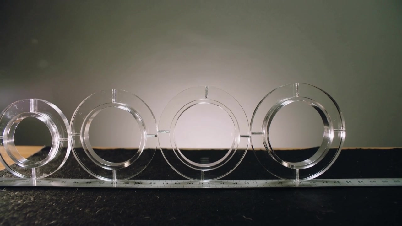 Shifting camera revealing leftmost ring and spacing to even composition on dark tabletop, ruler