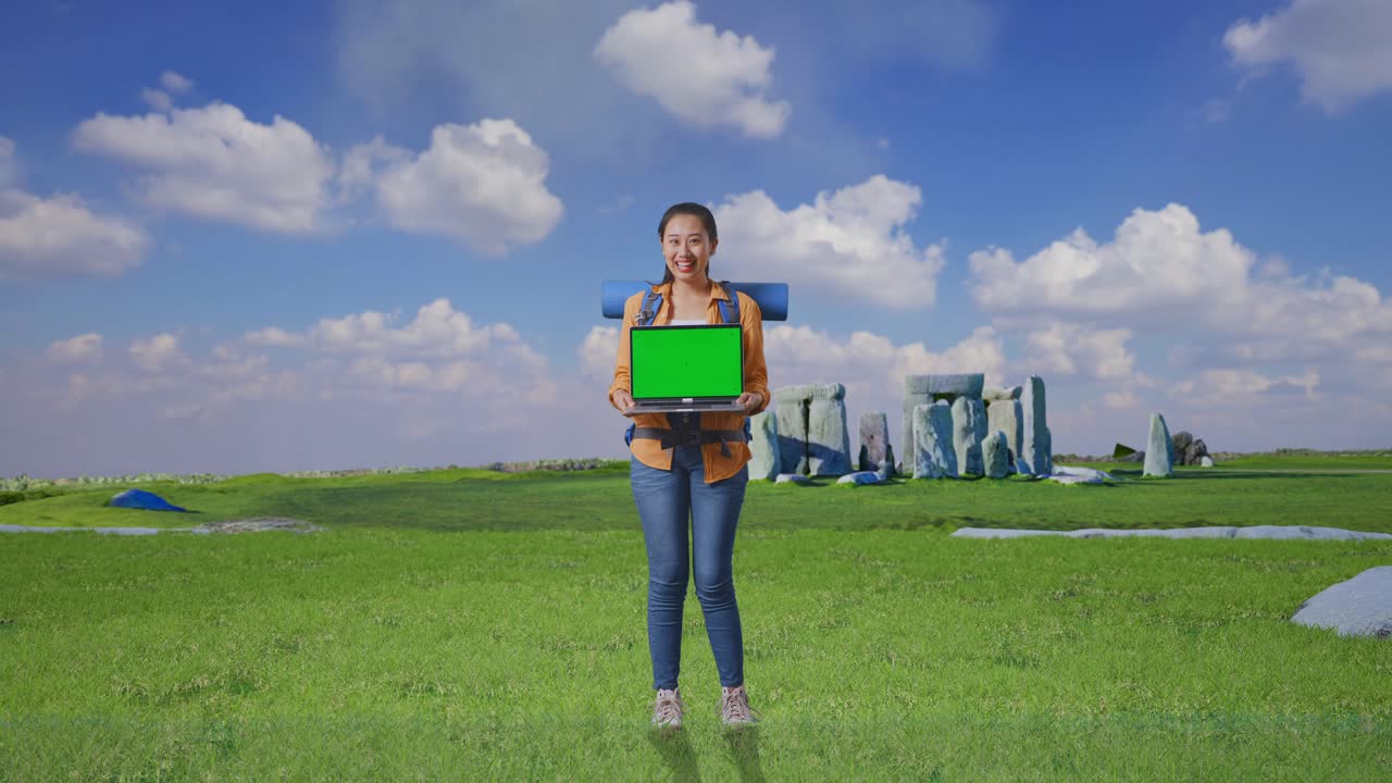 Full Body Of Asian Female Hiker With Mountaineering Backpack Smiling And Showing Mock Up Green Screen Laptop While Traveling In Stonehenge