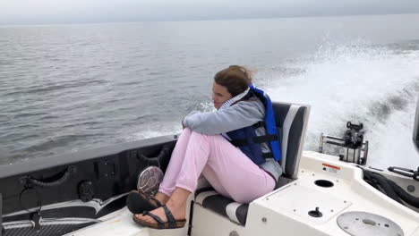 little girl riding in back of motor boat on lake