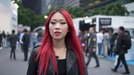 a young woman with striking red hair wears a black outfit while confidently walking through a crowded urban event. people are engaged in various activities around her in the modern setting.
