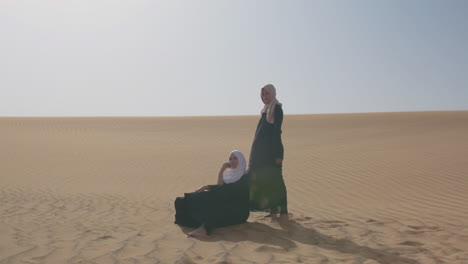 Two-Muslim-Women-Wearing-Traditional-Dress-And-Hijab-Posing-In-A-Windy-Desert