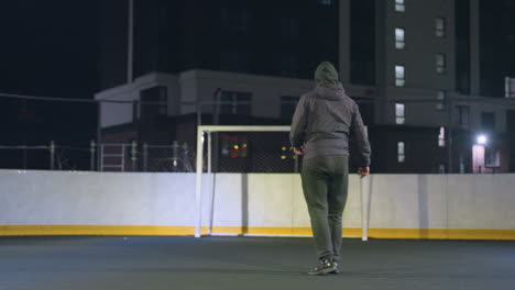 athlete skillfully kicks soccer ball into goalpost during night practice on urban outdoor field, residential building in background and illuminated setting