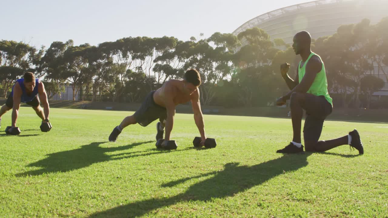 Diverse group of three fit men cross training doing press ups with weights outdoors