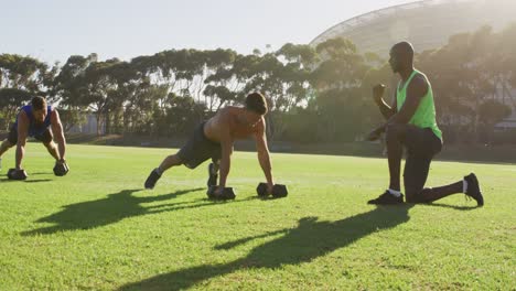 diverse group of three fit men cross training doing press ups with weights outdoors