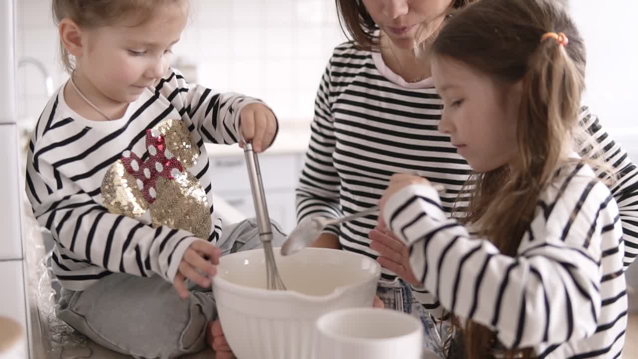 Daughters are kneading the dough with their mother on the kitchen
