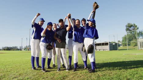 portrait of diverse team of female baseball players and coach on pitch, raising fists and cheering