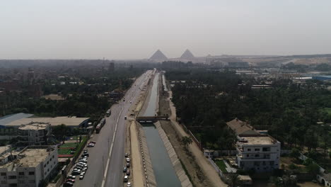 Aerial-Shot-Track-out-and-rising-up-for-The-Pyramids-of-Egypt-in-Giza-in-the-background-of-a-branch-of-the-River-Nile-in-the-foreground-Maryotya-branch-with-the-green-lands