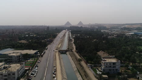 aerial shot track out and rising up for the pyramids of egypt in giza in the background of a branch of the river nile in the foreground maryotya branch with the green lands