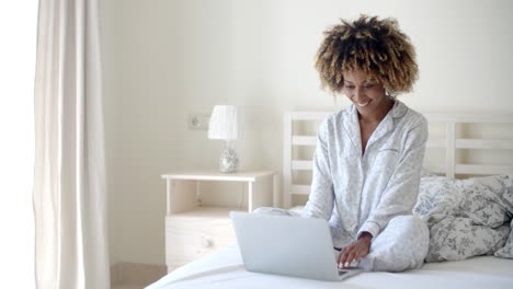 mujer joven que usa la computadora portátil en la cama