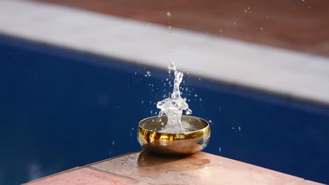 water falling fast and splashing in a small golden bowl in slow motion, creating a mesmerizing and tranquil scene