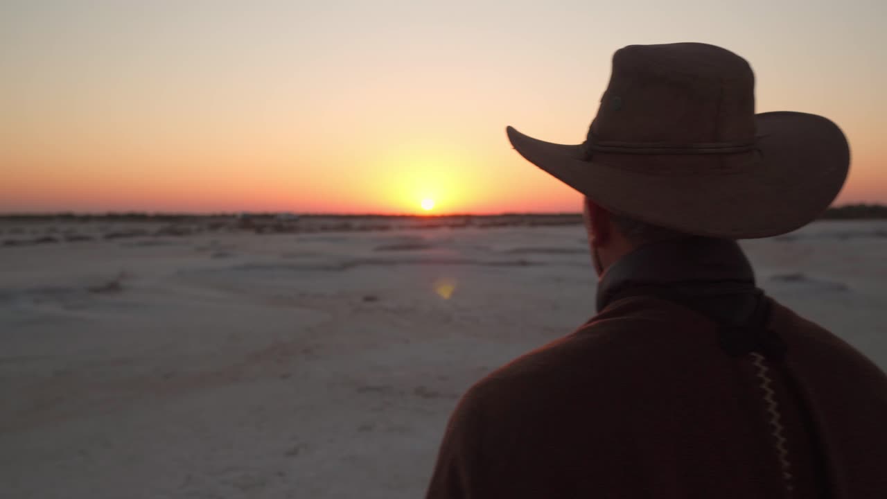 primer plano de un hombre vestido como un vaquero de pie en un campo de sal viendo el amanecer