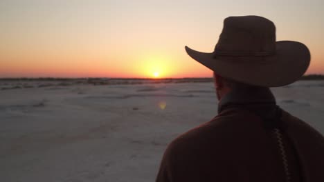 close up of a man dressed as a cowboy standing on a salt field watching the sunrise