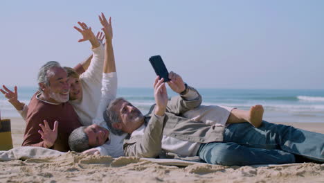 amigos mayores felices acostados en la orilla del mar y tomando selfies