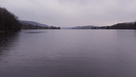 Dark,-moody-slow-motion-drone-shot-of-rain-falling-on-a-lake,-wide,-aerial